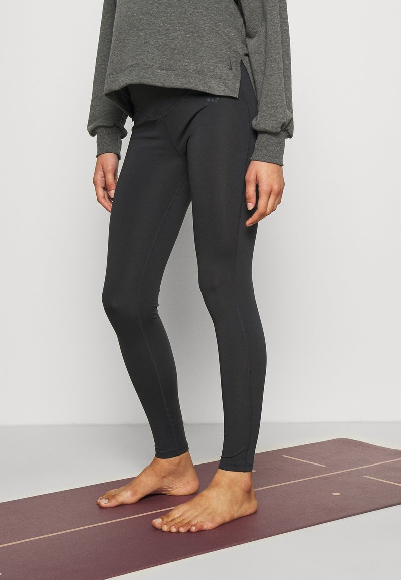 Černé sportovní legíny s hladkou texturou a přiléhavým střihem, doplněné šedým tričkem s dlouhým rukávem. Legíny mají jemné akcenty švů.