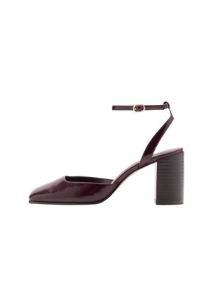 Zapato de tacón alto color púrpura oscuro con punta puntiaguda, tacón grueso y una correa en el tobillo con una pequeña hebilla dorada.