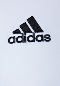 Biała tkanina z dużym czarnym logo Adidas, z trzema ukośnymi paskami nad nazwą marki wykonaną w mocnym haftem.
