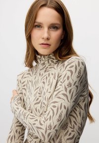 Camiseta de manga larga con cuello alto en beige con un patrón floral marrón, con un diseño ajustado y tela suave y elástica.