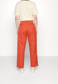 Hoge taille, wijde broekspijpen in levendig oranje katoen. Voorzien van twee achterzakken en een klein merklabel nabij de tailleband.