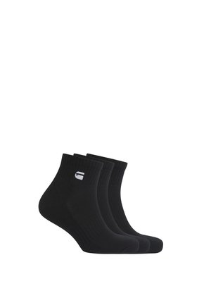 Trois paires de chaussettes noires courtes avec un petit logo blanc sur le côté, affichées sur un fond blanc.