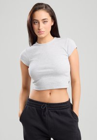 Harmaa ribbatuva cropped-top, jossa on hihattomat hihat ja tiukka muotoilu. Yhdistetty mustiin collegehousuihin, joissa on joustava vyötärönauha ja sivutaskut.