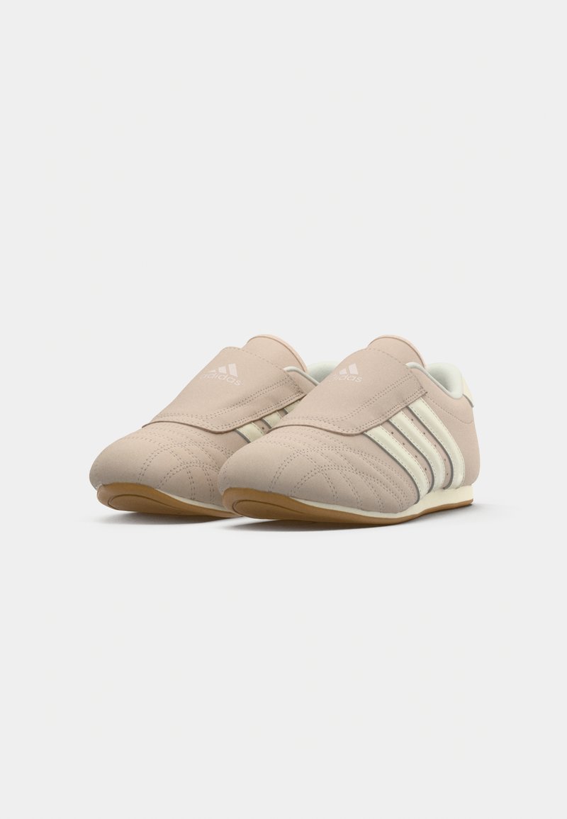 Par de zapatillas Adidas beige con rayas blancas y suelas de goma, que cuentan con una amplia correa de velcro en la parte superior.