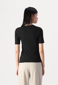 Top corto a maniche corte nero a coste con scollo rotondo, che aderisce bene al corpo. Indossato con pantaloni chiari e larghi.