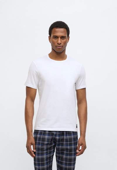 Balta īsroku T-krekls ar apaļu kakla izgriezumu, izgatavots no gludas auduma. Kombinēts ar zilām un melnām pleda raksta biksēm.