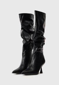 Zwarte leren kniehoge laarzen met een slouch-design, puntige neus en een smalle stilettohak. Voorzien van een zijrits. Glad oppervlak.