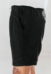 Shorts negros de tela texturizada, con una cintura elástica, bolsillos laterales y un corte a la altura de la rodilla. Diseño liso sin patrones.