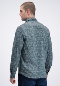 Herenoverhemd met lange mouwen in een teal kleurige stof met een geometrisch patroon. Voorzien van een knoopsluitbare kraag en manchetten. Soepele textuur.