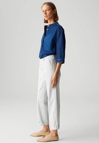 Chemise en jean à boutons de couleur bleu foncé, manches trois-quarts ; pantalon blanc à revers ; ballerines beige à bout pointu, design minimaliste, texture lisse.