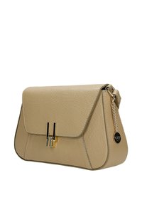 Béžová texturovaná kožená kabelka přes rameno s klopou, zlatou a černou kovovou sponou a řetízkem s kulatým černým přívěskem s logem na straně.