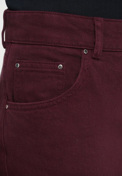 Pantalones de mezclilla burdeos con costuras visibles, un pequeño bolsillo y herrajes en tono plateado. Textura suave con un diseño de cintura ajustada.