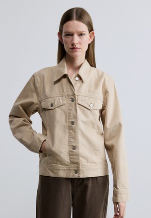 Giacca di jeans beige con collo a risvolto, maniche lunghe, chiusura frontale con bottoni e due tasche sul petto con bottoni in metallo.