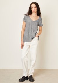 Pilkos spalvos trumpomis rankovėmis V formos iškirptės marškinėliai, derinami su baltais, laisvai krentančiais džinsais ir juodais aulinukais. Slygi medžiaga; atsipalaidavęs siluetas.