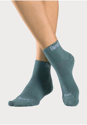 Feet wearing teal ankle socks with "Bench" branding on cuffs and "Sport" text near toes, against a plain light background.