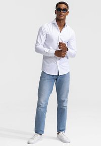 Witte overhemdd met lange mouwen, lichtblauwe jeans en witte sneakers, gecombineerd met donkere zonnebril. Eenvoudig ontwerp en getailleerde pasvorm.