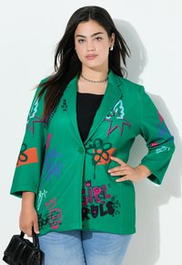 Groene blazer met abstracte graffiti-patronen in roze, zwart en oranje. Voorzien van een enkele knoopsluiting en een losse, oversized pasvorm.