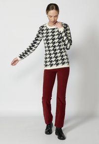 Pulover cu model houndstooth alb-negru, fabricat din tricot moale, asortat cu pantaloni din catifea burgundă și cizme negre cu șiret.