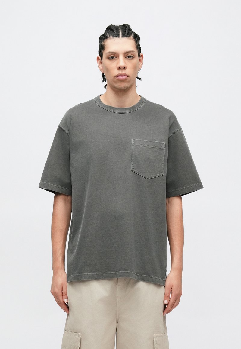 Grå oversize T-shirt i bomull med rund hals och korta ärmar. Har en bröstficka och synliga söm detaljer.