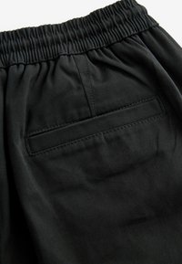Pantalons noirs avec une taille élastique, dotés d'une poche arrière avec un rabat rectangulaire. Fabriqués à partir d'un tissu lisse et durable avec une finition mate.