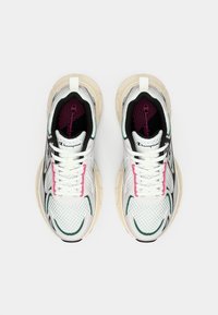 Fehér sportcipők légáteresztő felsőrésszel, fekete és zöld díszítéssel, valamint rózsaszín részletekkel. Vastag bézs talpak és lapos fehér fűzők.