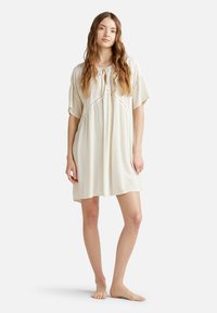 Camisa de noche ligera en marfil con un corte relajado, mangas cortas y un escote en forma de ojo de cerradura. Presenta una tela texturizada y una silueta fluida.