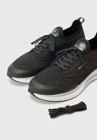 Černé sportovní boty s texturovanou tkaninou, šněrovacím designem a bílou mezipodeševí s jemným duhovým akcentem. Součástí jsou také extra černé tkaničky.