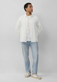 Witte overhemd met verticale strepen, gecombineerd met lichtblauwe jeans en casual grijze sneakers. Gladde textuur, relaxte pasvorm.