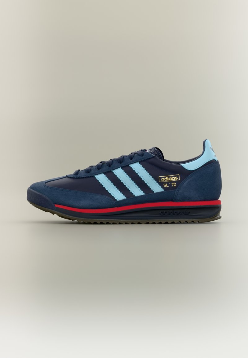 Marineblaue Wildleder- und Sneakers aus Synthetik mit drei hellblauen Streifen, schwarzer Außensohle und roter Zwischensohle. Goldfarbenes Logo-Detail an der Seite. Klassisches Design.