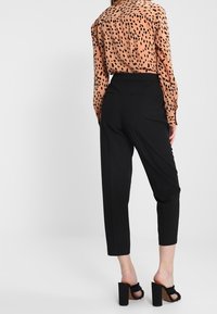 Brun skjorta med svarta leopardfläckar, svarta skräddarsydda byxor och svarta klacksandaler med en texturerad rem och träplattform.