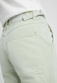 Jeans en denim vert clair avec des coutures angulaires et des poches arrière. Présente une étiquette blanche BZB sur la taille.