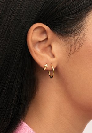 Pendientes de aro dorados acompañados de un pequeño acento en forma de estrella; acabado metálico brillante, formas circulares y de estrella, complementan diversos estilos.