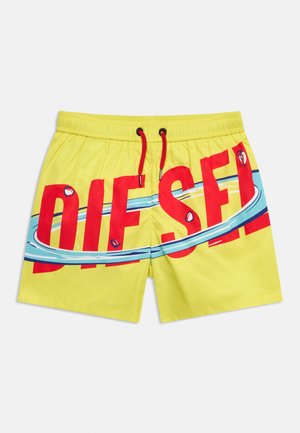 Žlté plavkové šortky s červeným šnúrkou na stiahnutie a veľkým červeným nápisom "DIESEL", ktorý je čiastočne obklopený modro-bielym vlnovým motívom cez prednú časť.