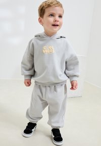 Hall hall kapuutsiga dressipluus kirjaga "COOL VIBES", sobivate hallide dressipükstega ja mustade velkrotossudega. Pehme materjal, mugav ja lõdvestunud lõige, soonikkoes mansetid.