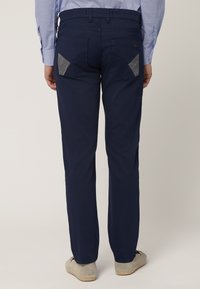 Pantalones azul marino con bolsillos traseros en forma de diamante gris en contraste, cintura plana y diseño de pierna recta. Textura de tela suave.
