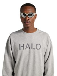 Mężczyzna noszący białe okulary przeciwsłoneczne typu wraparound i szarą bluzę z dużym napisem „HALO” z przodu.