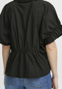Black elastic waist top with puffed sleeves, made from lightweight fabric, featuring a gathered design and a peplum silhouette.