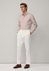 Chemise boutonnière rose clair avec un tissage texturé, assortie à un pantalon droit blanc. Des chaussures en cuir marron complètent la tenue.