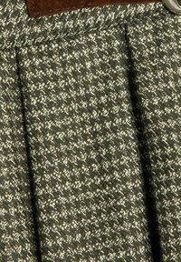 Groene textuurstof met een geweven patroon, met lichte en donkere draden. Bruin leren accent met een zilveren gesp detail.