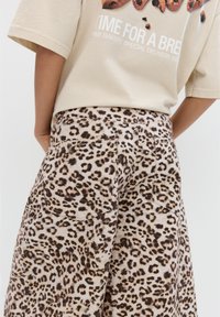 Tricou bej cu un grafic de biscuit și text, asortat cu o fustă cu imprimeu leopard de culoare maronie, care dispune de buzunare la spate și un material texturat.