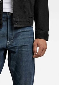 Czarna kurtka dżinsowa w połączeniu z niebieskimi jeansami z kontrastującymi przeszyciami. Kurtka ma zapięcie na guziki i dopasowany krój.