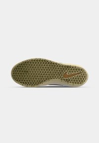 Semelle de chaussure avec motif de bande de roulement texturé et logo Nike swoosh près du talon en brun sur fond beige clair.