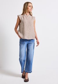 Blusa a strisce senza maniche in tessuto beige e bianco con colletto; abbinata a jeans in denim azzurro chiaro a gamba larga e scarpe nere intrecciate.