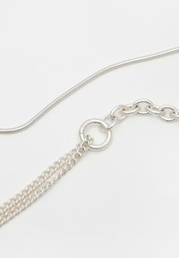 Dva strieborné náhrdelníky s rôznymi štýlmi prepojení spojené kruhovou sponou na bielom pozadí.