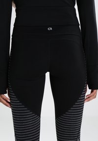 Czarne legginsy z teksturowanym materiałem, z solidnymi, czarnymi i szarymi paskami. Pasek w talii jest elastyczny z detalem logo.