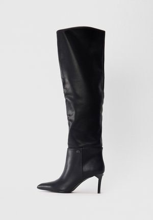 Schwarze Lederstiefel über das Knie mit spitzem Schuh und Stiletto-Absatz, die ein elegantes Design mit einem Logo-Detail am Knöchel aufweisen.