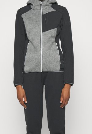 Lange mouwen zip-up hoodie met grijs gestructureerd voorpaneel, zwarte mouwen en zijkanten, ritssluitingen in zakken, gedragen met zwarte broek.
