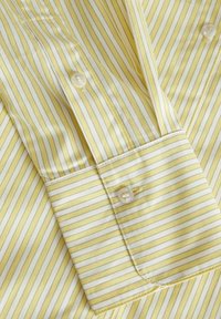 Camicia a righe gialle con sottili strisce bianche, chiusura con bottoni con finitura perlacea e una texture di tessuto liscia e leggera.