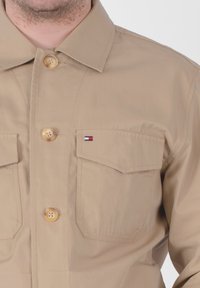 Camicia beige con bottoni, realizzata in tessuto liscio, dotata di due tasche sul petto con un accent logo e grandi bottoni rotondi.