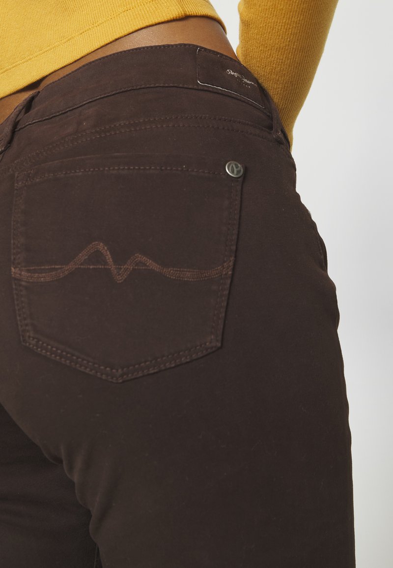 Braune Jeans mit einer schmalen Silhouette, ausgestattet mit einer Gesäßtasche mit einer wellenförmigen Naht und einem Metalllogo-Button.